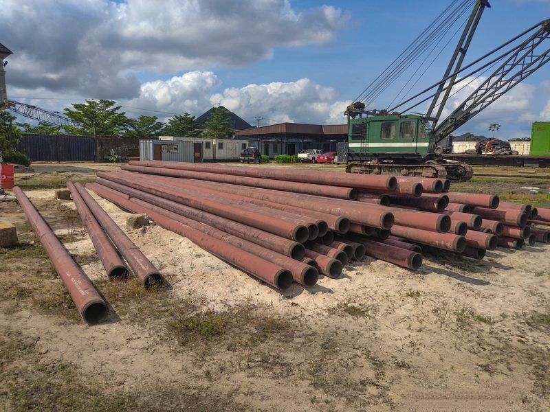 Lengths of rusted pipe laid on dirt in a yard