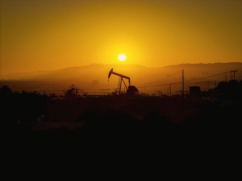 A pumpjack small against a hazy orange sun
